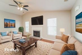 Charlotte house for rent - A living room with a fireplace, a couch, a chair, a coffee table, a plant, a painting, a television, and a ceiling fan.