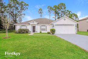 Palm Coast house for rent - A white house with a brown roof and a garage door is surrounded by a grassy lawn and trees.