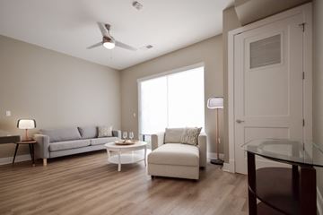 Rochester Hills apartment for rent - A living room with a grey couch, a white couch, a glass table and a wooden floor.
