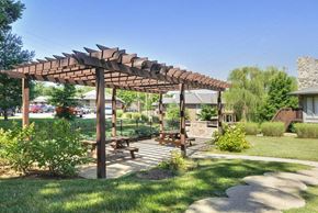 Louisville apartment for rent - A wooden pergola with a bench underneath it is situated in a grassy area.