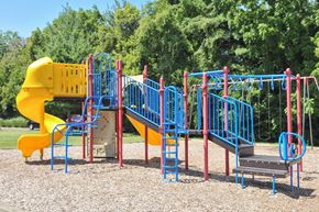 Louisville apartment for rent - A playground with a yellow slide, blue and red climbing structures, and a grey platform.