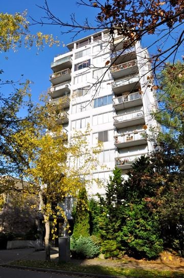 Vancouver apartment for rent - A tall white building with balconies is surrounded by trees.