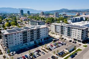 Kelowna apartment for rent - A parking lot in front of apartment buildings with a lake and mountains in the background.