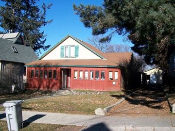 Pullman apartment for rent - A red building with green shutters sits in front of a tree.