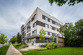 Waterloo apartment for rent - A modern building with a flat roof and large windows is surrounded by a well-kept lawn and trees.