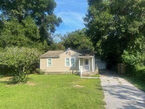Pensacola house for rent - A small house with a porch is surrounded by trees.