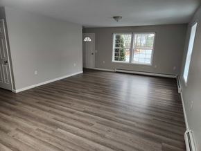 Gray apartment for rent - A room with wooden flooring and a window with a view of a tree.