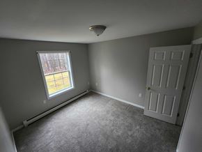 Gray apartment for rent - A room with a carpeted floor, a white door, and a window with a view of a building outside.