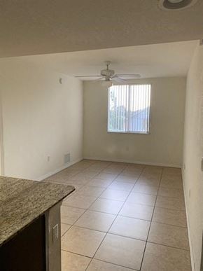 Miami apartment for rent - an empty living room with a ceiling fan and tiled floor