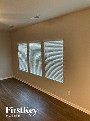Charlotte house for rent - A room with wooden floors and three windows covered with white blinds.