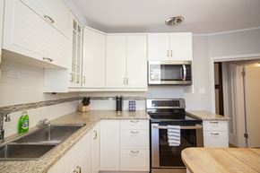 Winnipeg triplex for rent - a kitchen with white cabinets and granite counter tops and black appliances