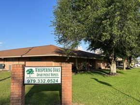 El Campo apartment for rent - A sign for Whispering Oaks Apartment Homes stands in front of a building.