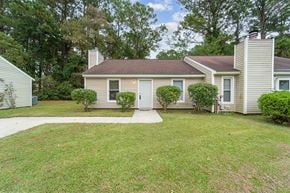 Jacksonville house for rent - A house with a brown roof and a white door is surrounded by a green lawn.