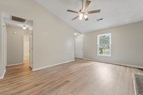 Jacksonville house for rent - A room with a ceiling fan and light, hardwood floors, and a window showing a view of a tree and a building.