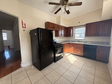 Cranford apartment for rent - A black refrigerator in a kitchen with brown cabinets and a ceiling fan.