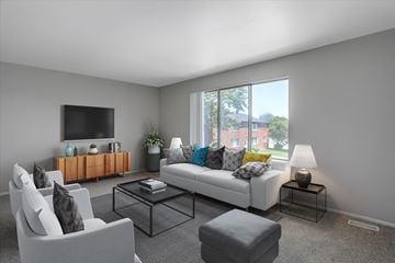 Sterling Heights apartment for rent - A living room with a white couch, a grey armchair, a glass coffee table, and a television on the wall.