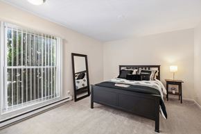 Williamston apartment for rent - A bedroom with a large bed, a nightstand, and a window with blinds.