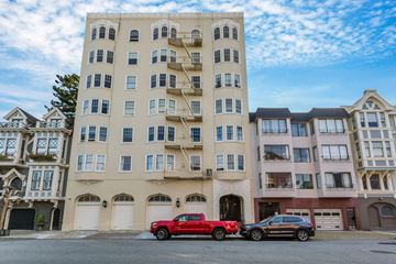 San Francisco apartment for rent - A red truck is parked in front of a beige building with a black car behind it.