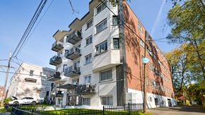 Montréal apartment for rent - A multi-story building with a mix of white and brick facades, featuring balconies and windows.