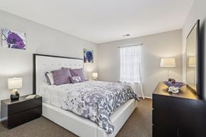 Monmouth Junction apartment for rent - A bedroom with a large bed and a nightstand with a lamp.