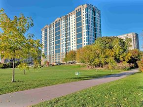 Ottawa apartment for rent - A tall building with many windows is surrounded by trees and a grassy area.