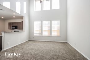 Splendora house for rent - A spacious room with a carpeted floor and a kitchen area in the background.