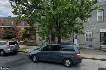 Baltimore house for rent - A street view with a car and a tree in front of a building.