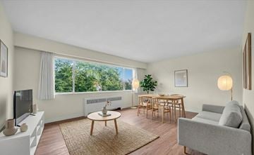 Vancouver apartment for rent - A living room with a grey couch, a wooden coffee table, a television, and a window with a view of trees.