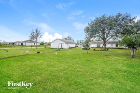 Lehigh Acres house for rent - A grassy field with a white house and trees in the background.