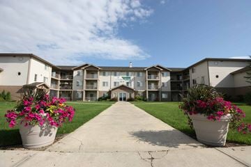 Red Deer apartment for rent - A building with a walkway in front and two large pots of flowers on the sides.