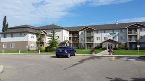 Red Deer apartment for rent - A blue car is parked in a parking lot in front of a building.