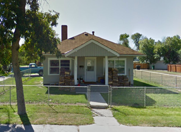Great Falls house for rent - A small house with a brown roof and a white door is surrounded by a fence.