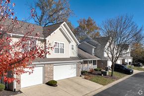 Indianapolis townhouse for rent - A house with a white garage door is surrounded by trees and a black car is parked in the driveway.