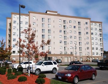 Kitchener apartment for rent - A red car is parked in front of a large apartment building.