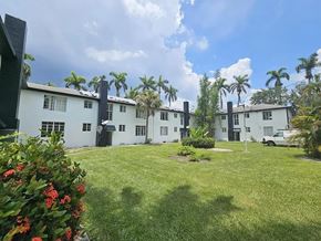 Fort Myers apartment for rent - A white building with a green lawn in front and palm trees in the background.