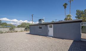 Tucson house for rent - A small grey building with a white door and a window is surrounded by a gravel lot.