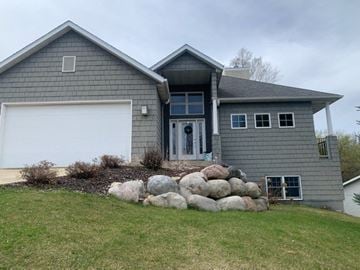 Rochester house for rent - A grey house with a white garage door and a stone wall in front.