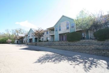 Rochester apartment for rent - A large building with a blue and white exterior is surrounded by a stone wall and a tree.