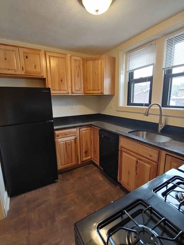 Pittsburgh apartment for rent - A black fridge and stove in a kitchen with wooden cabinets.