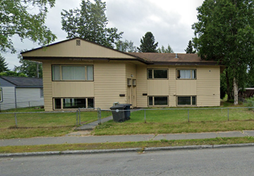 Anchorage apartment for rent - A beige house with a black trash can in front of it.