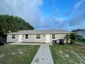 Lake Worth apartment for rent - A house with a white door and windows is surrounded by a grassy area and trees.