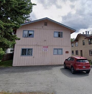 Anchorage apartment for rent - A red car is parked in front of a pink building with a sign on it.