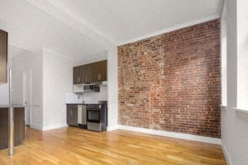 New York apartment for rent - an empty living room with a brick wall and a kitchen