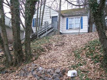 Pullman apartment for rent - A small house with a blue and white exterior is surrounded by trees and a stone wall.