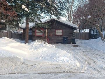 Anchorage apartment for rent - A wooden cabin with a red wreath on the window is surrounded by snow.