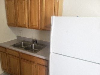 Anchorage apartment for rent - A white refrigerator stands next to a kitchen sink with wooden cabinets above it.