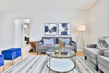 Mississauga apartment for rent - A living room with a grey couch, a blue ottoman, a glass coffee table and a painting on the wall.