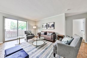 Mississauga apartment for rent - A living room with a grey couch, a blue ottoman, and a round glass table.