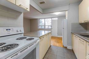 Mississauga apartment for rent - A white stove top oven sits in a kitchen with white cabinets and a window.