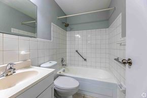 Brampton apartment for rent - A white toilet sits next to a white bathtub in a bathroom.